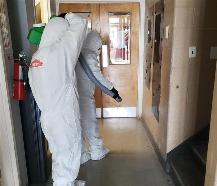 Two SERVPRO employees in white hazmat suits in a hallway. 
